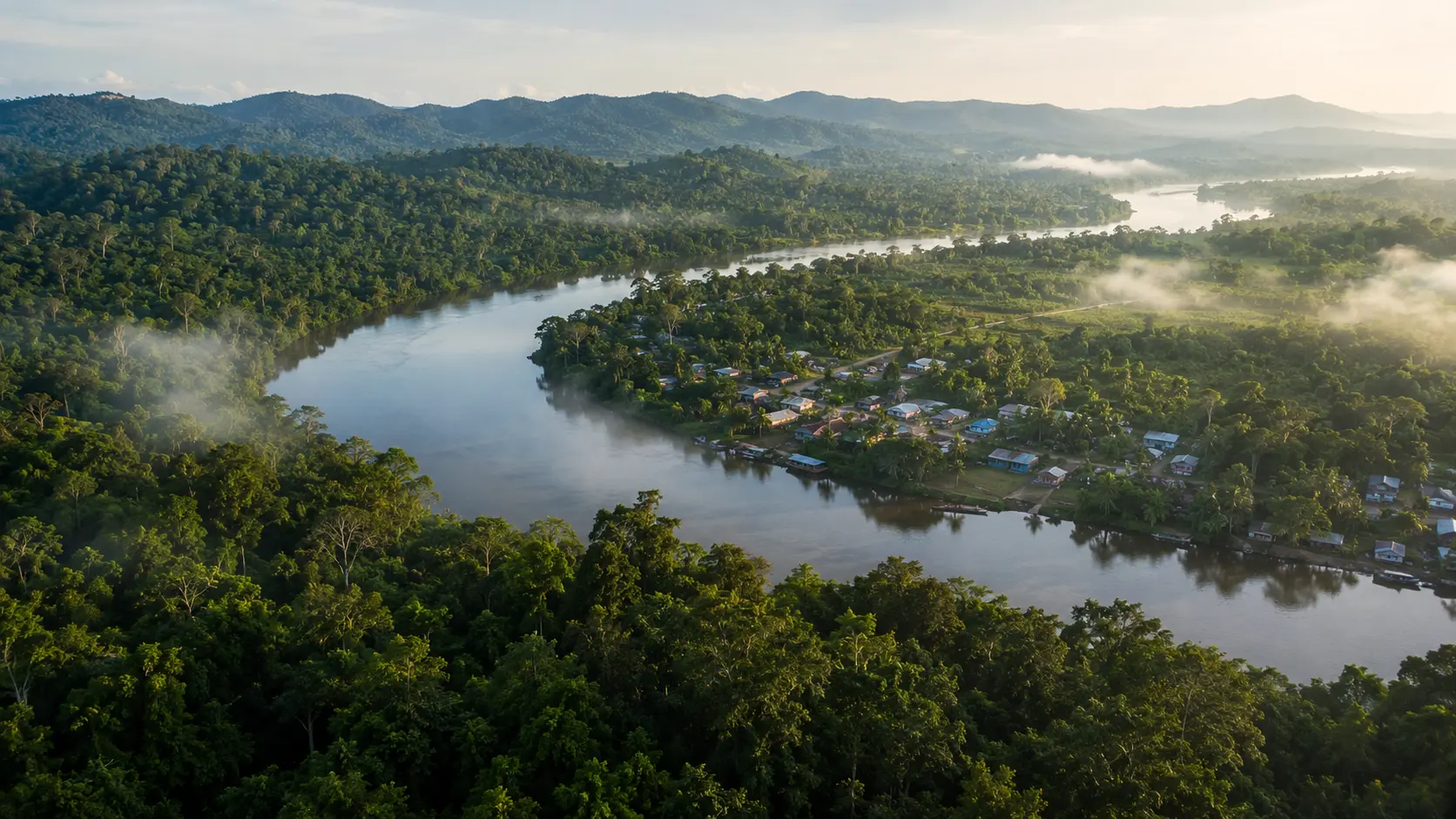 Aerial view of a river, a small village, and dense tropical rainforest in the morning mist.